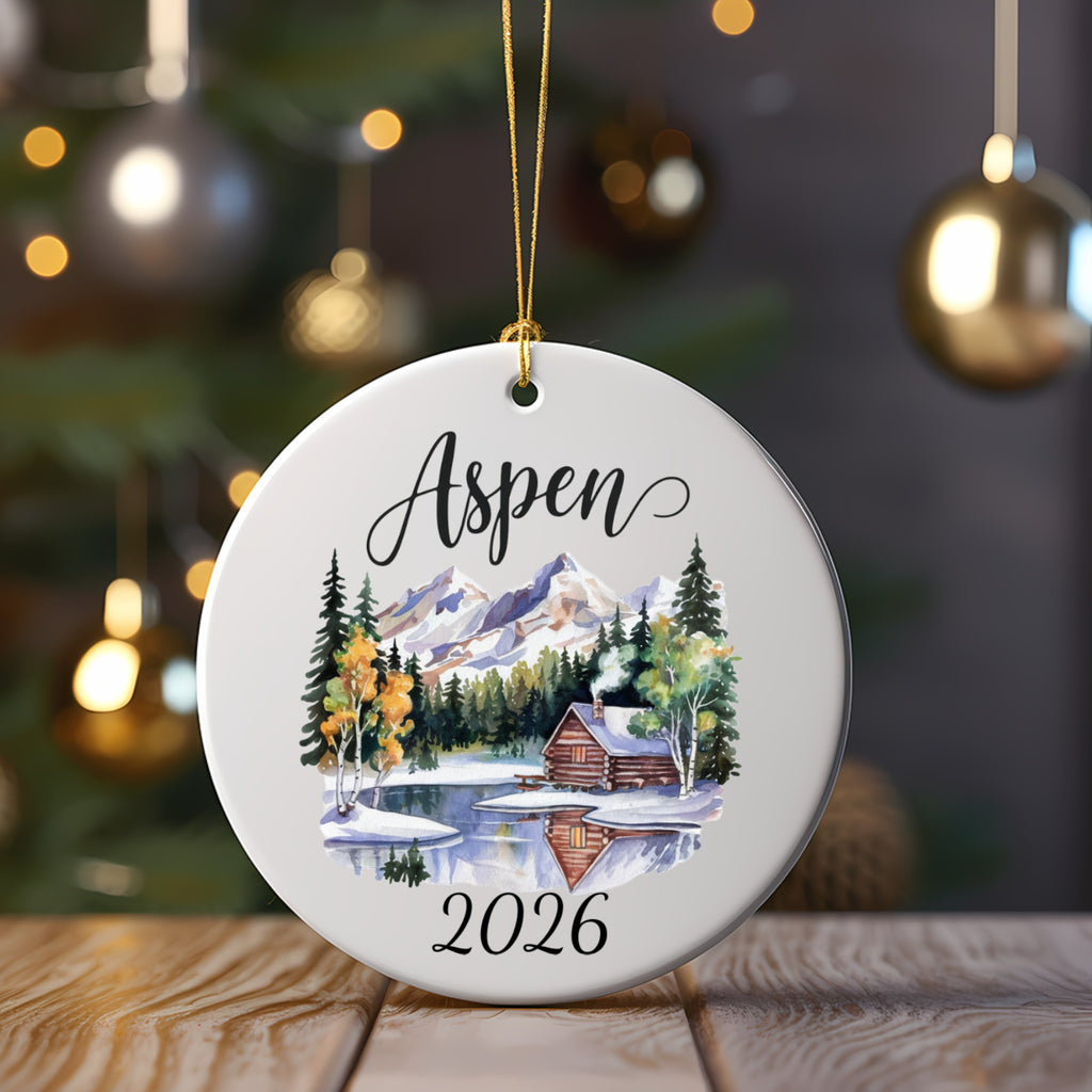 Round ornament with "Aspen 2026" and a winter cabin scene.