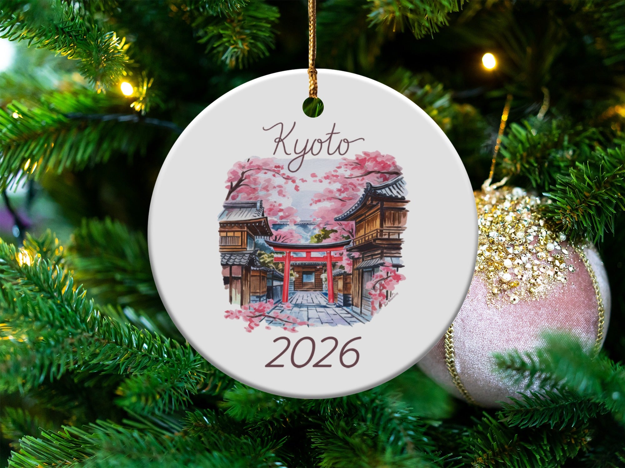 Round ceramic ornament with Kyoto 2026 design hangs on Christmas tree.