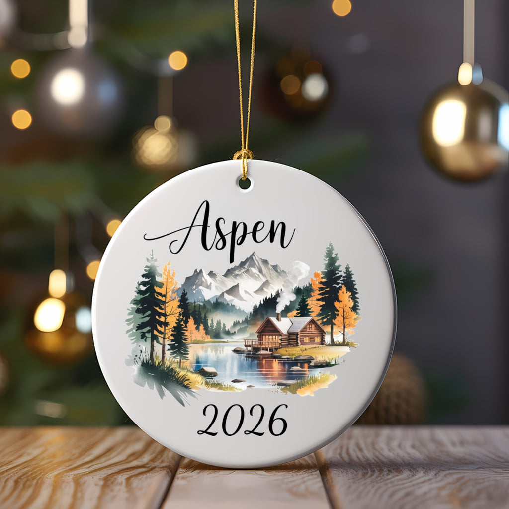 Round ornament with "Aspen 2026" and a mountain cabin scene.
