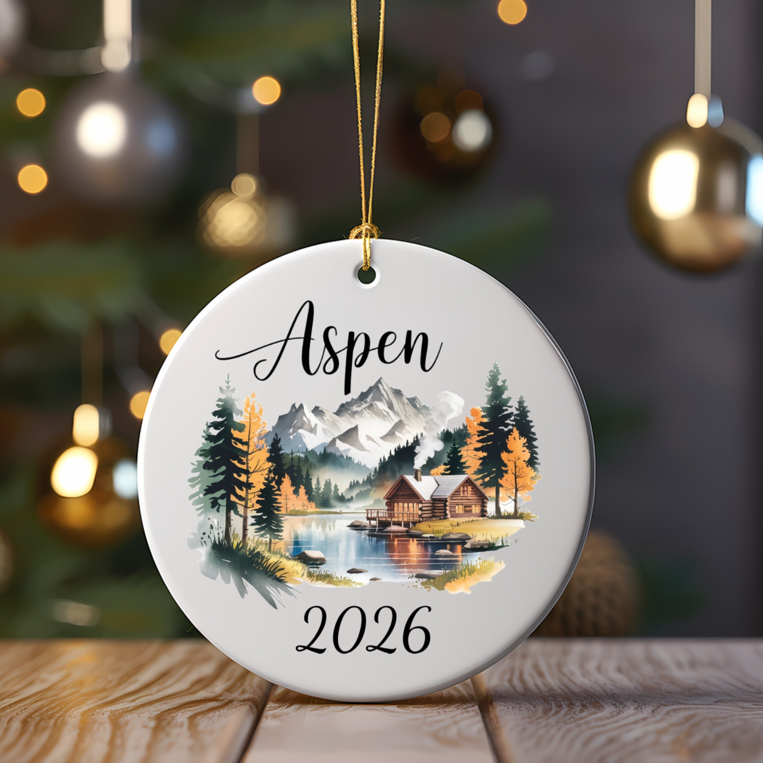 Round ornament with "Aspen 2026" and a mountain cabin scene.