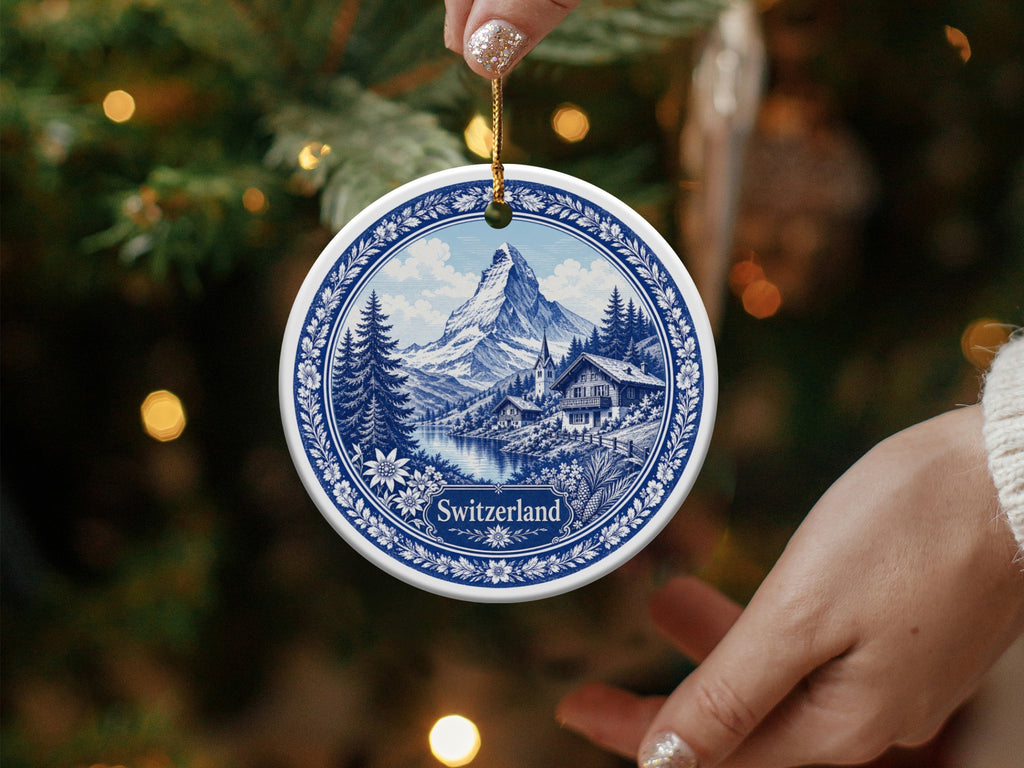 Round ornament with blue and white Swiss mountain village scene and "Switzerland" text.
