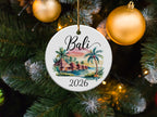 Round ornament with tropical beach scene, palm trees, and "Bali 2026" text.