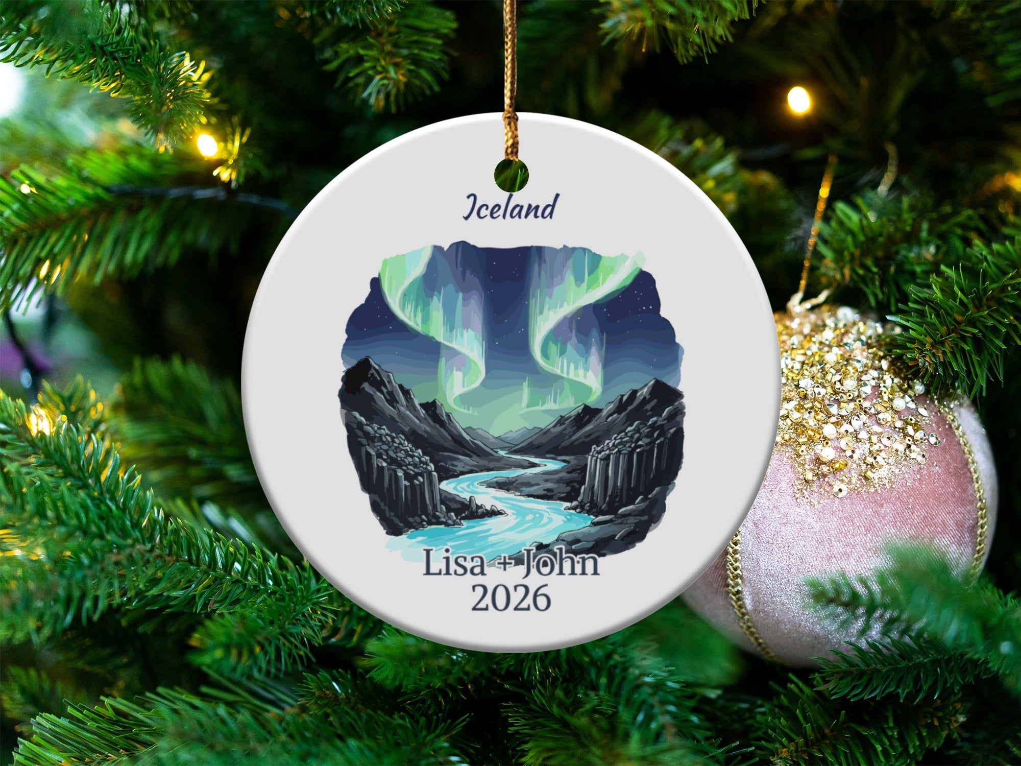 Round ceramic ornament with Iceland northern lights, river, and "Lisa + John 2026" text.