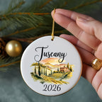 Round ceramic ornament with a Tuscan landscape and "Tuscany 2026" text.