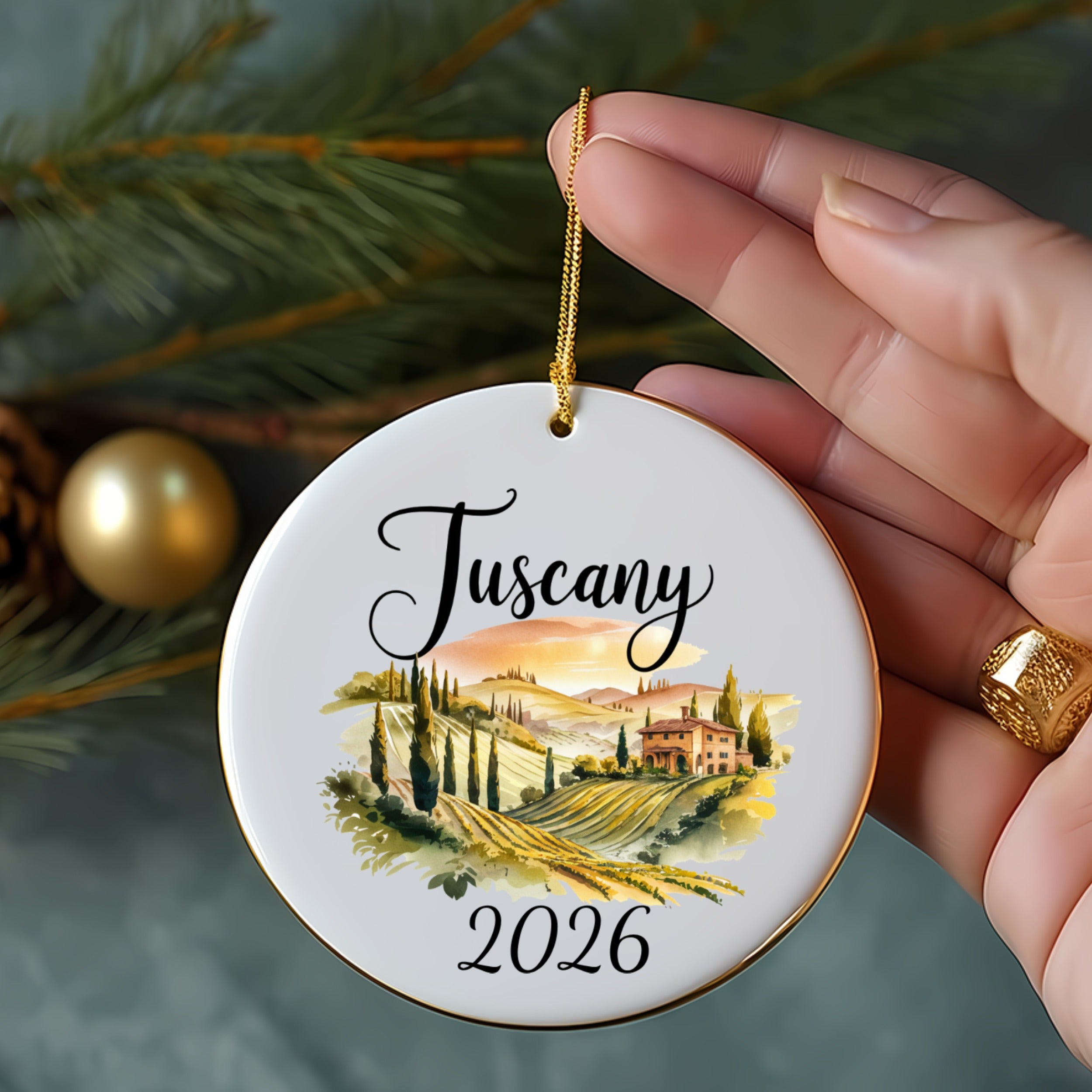 Round ceramic ornament with a Tuscan landscape and "Tuscany 2026" text.