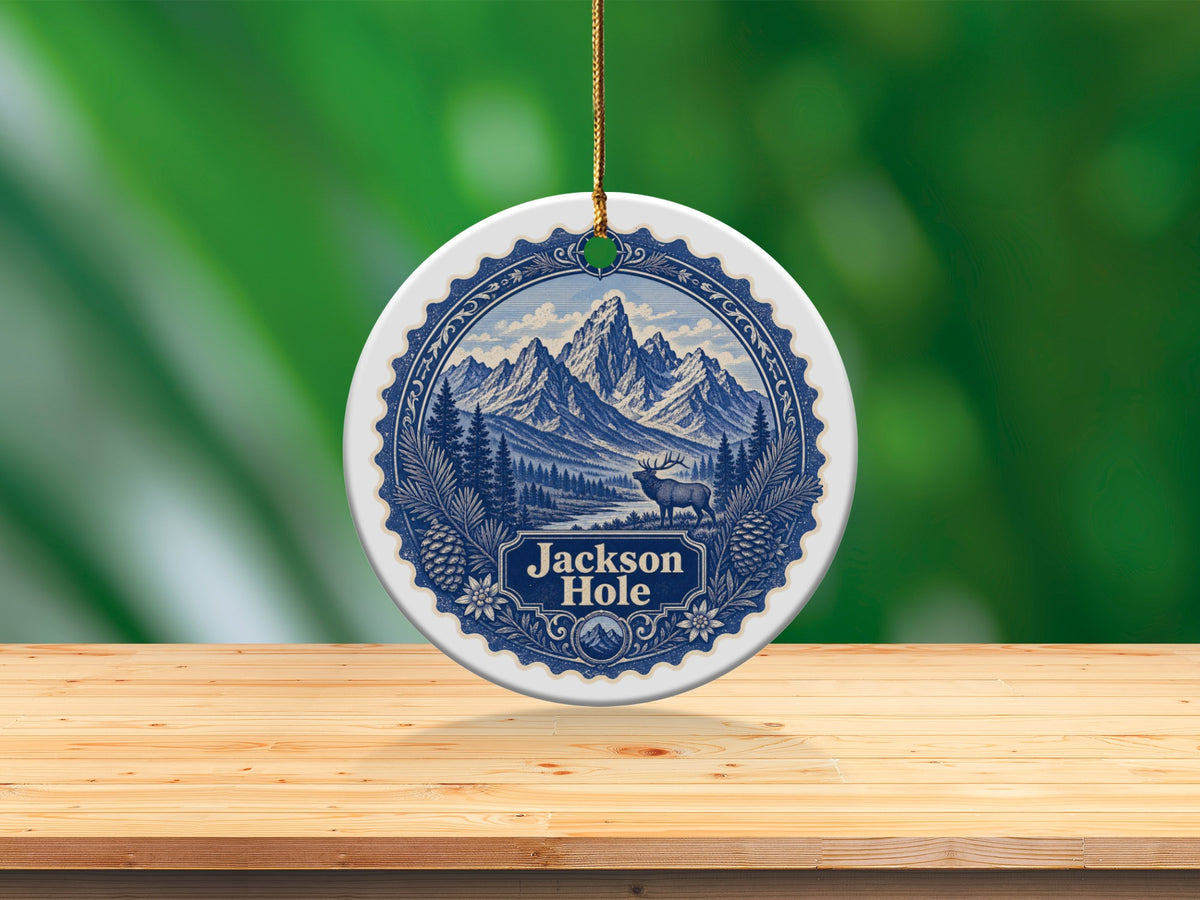 Round Jackson Hole ornament with mountain landscape and elk on a wooden surface.