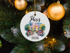 Round ceramic ornament with "Paris 2026" and Parisian street scene illustration.