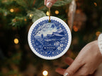 Round ceramic ornament with blue and white Kyoto, Japan scene, held near a Christmas tree.