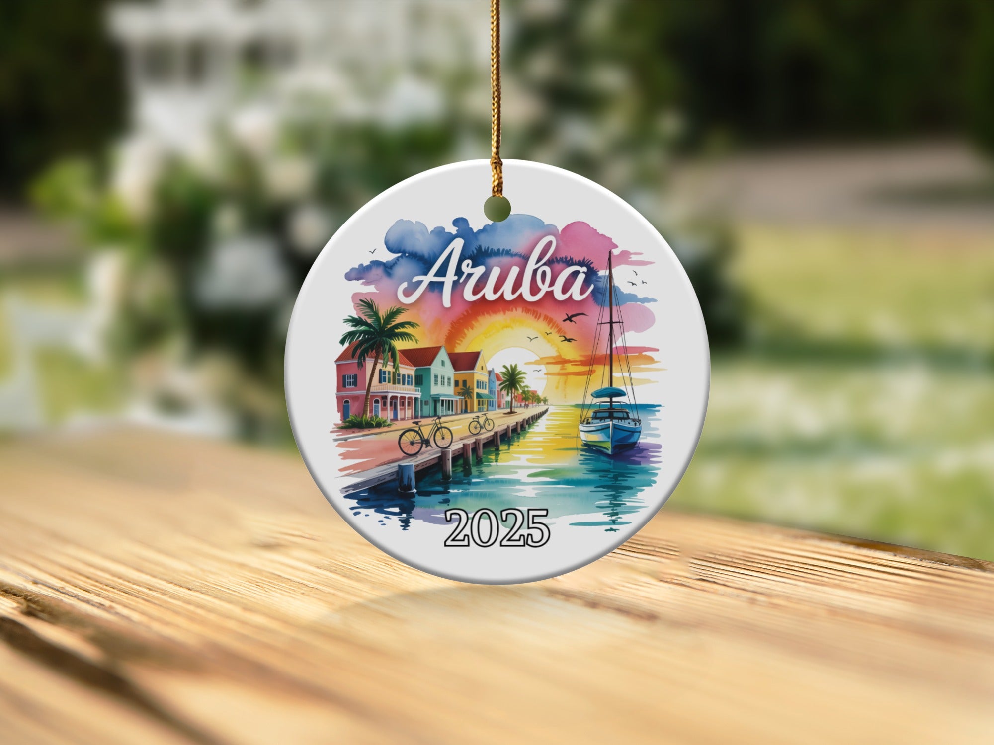 Round ornament with watercolor scene of Aruba: beach, buildings, boat, and "2025".