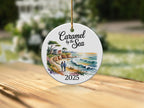 Round ceramic ornament with a coastal landscape and "2025" at bottom.