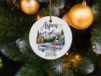Circular ornament with "Aspen 2026" above a cabin scene and snow-capped mountains.