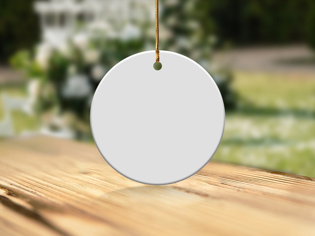 Blank white ceramic circle ornament hanging on gold string over wooden surface.