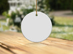 Blank white ceramic circle ornament hanging on gold string over wooden surface.