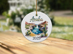 Round ceramic ornament with "Aruba 2025" and a desert oasis scene.