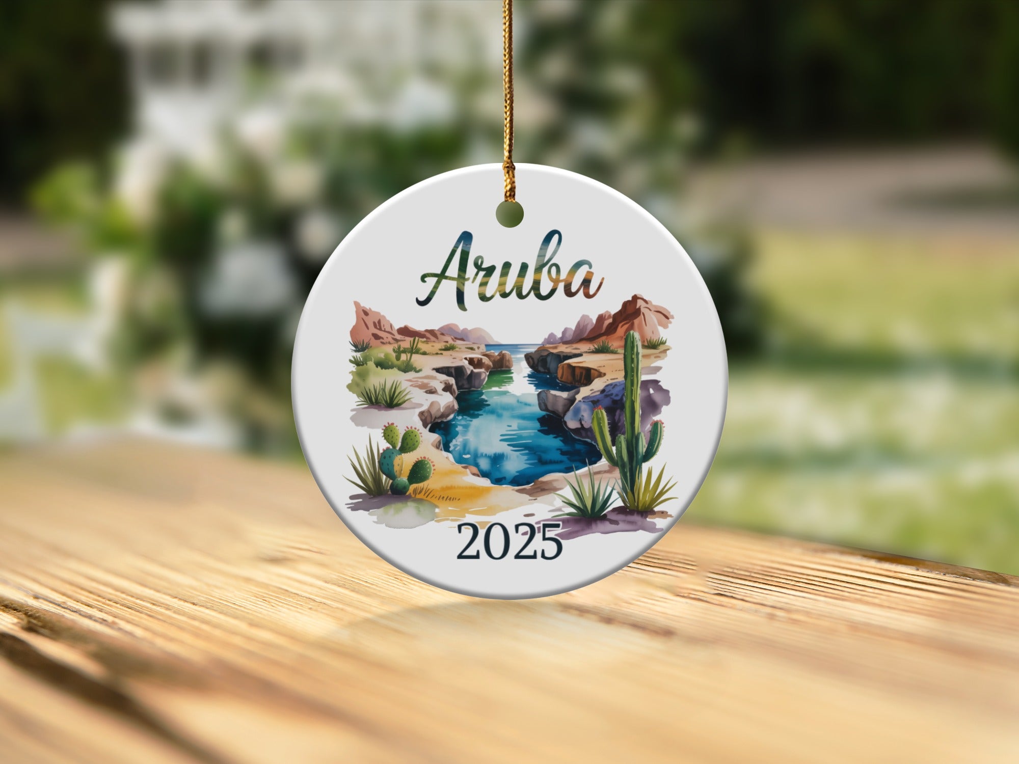 Round ceramic ornament with "Aruba 2025" and a desert oasis scene.