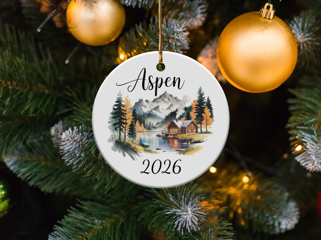 Round ornament with a winter cabin scene and "Aspen 2026" text.