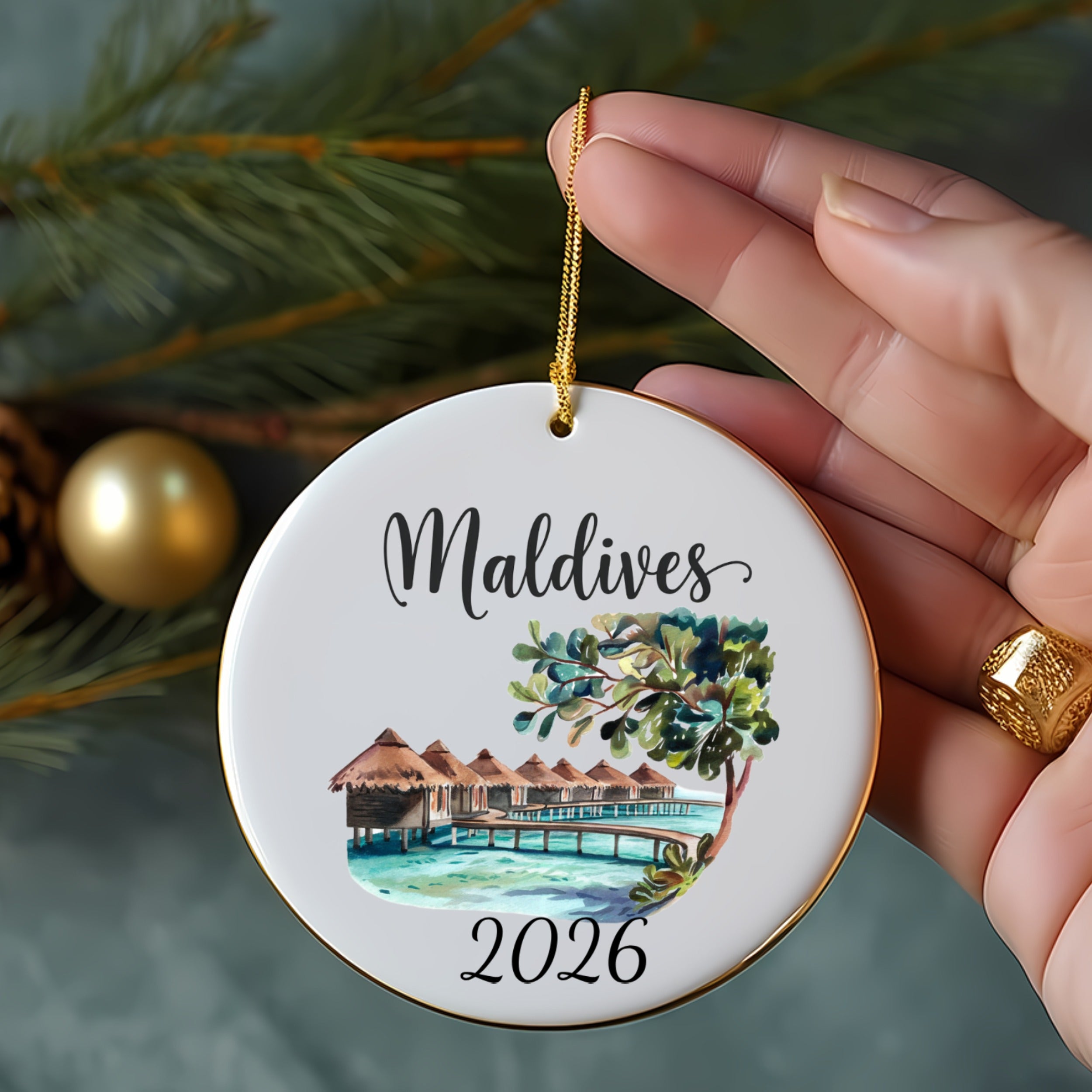 Round ornament with "Maldives" and "2026" above a watercolor scene of huts on stilts.