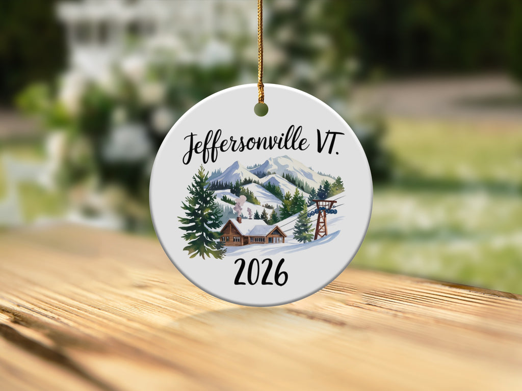 Round ceramic ornament depicting Jeffersonville VT 2026 with ski slopes and cabins.