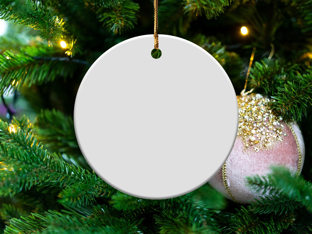 Blank round ceramic ornament hanging on a decorated Christmas tree.